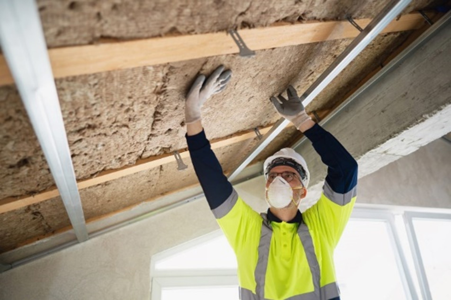 A person wearing a mask and gloves working on a ceiling