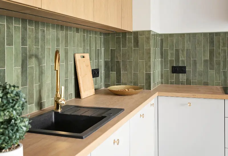 A close-up of a sink and green tile backsplash after a kitchen was remodeled