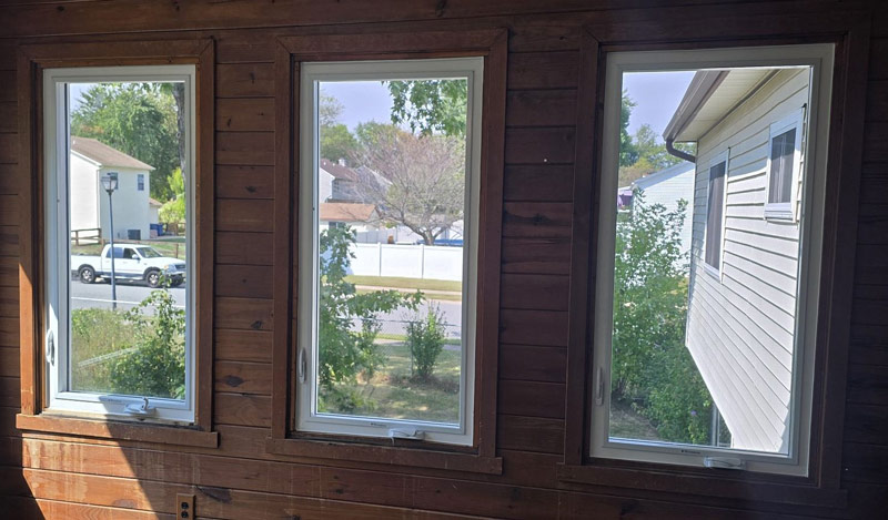 Three windows framed in wood with a view of houses and trees outside.