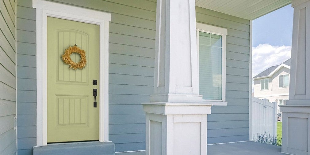 House front porch featuring a light green door with a decorative wreath, light blue-gray siding, and white trim